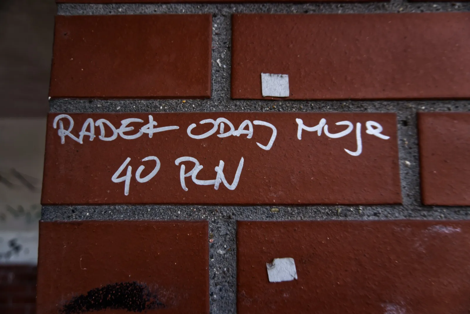Zdjęcie napisu wykonanego na ścianie wiaty przystankowej, wykonanej z cegły. Napis głosi "Radek oddaj moje 40 PLN".